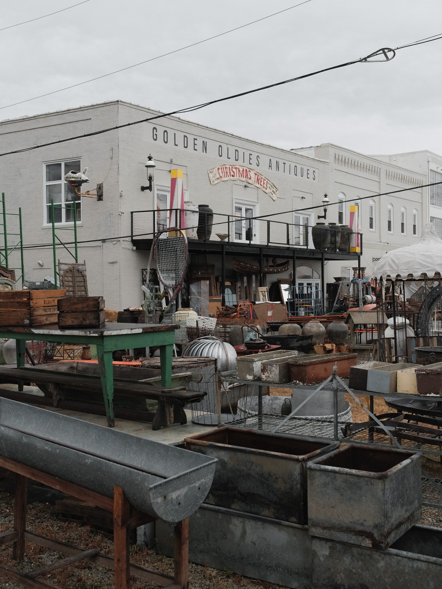 Exterior shot of Golden Oldies Antiques featuring vintage industrial bins, tables, and pottery